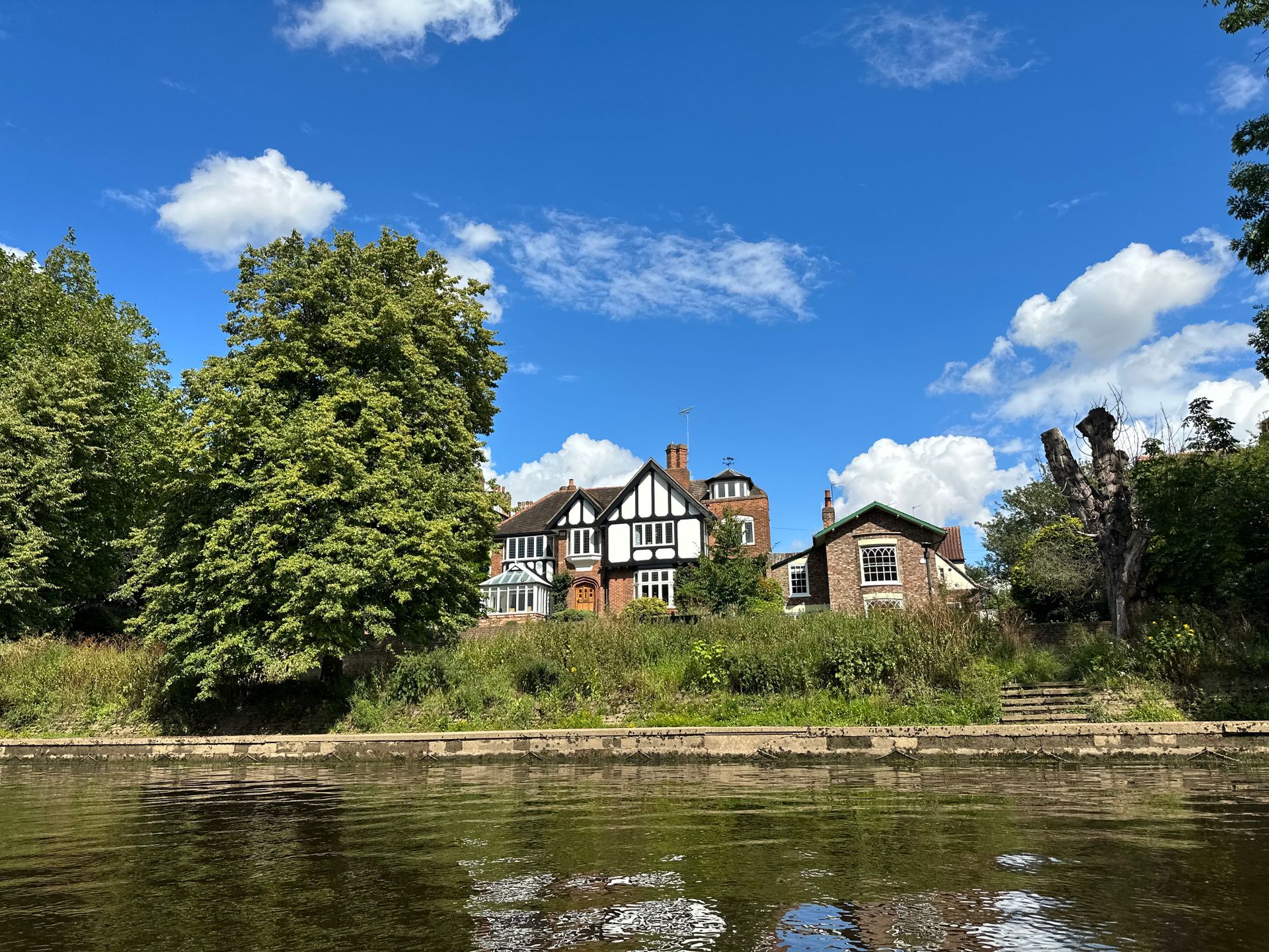 Picturesque Tudor house on a sunny day by the river with lush greenery.