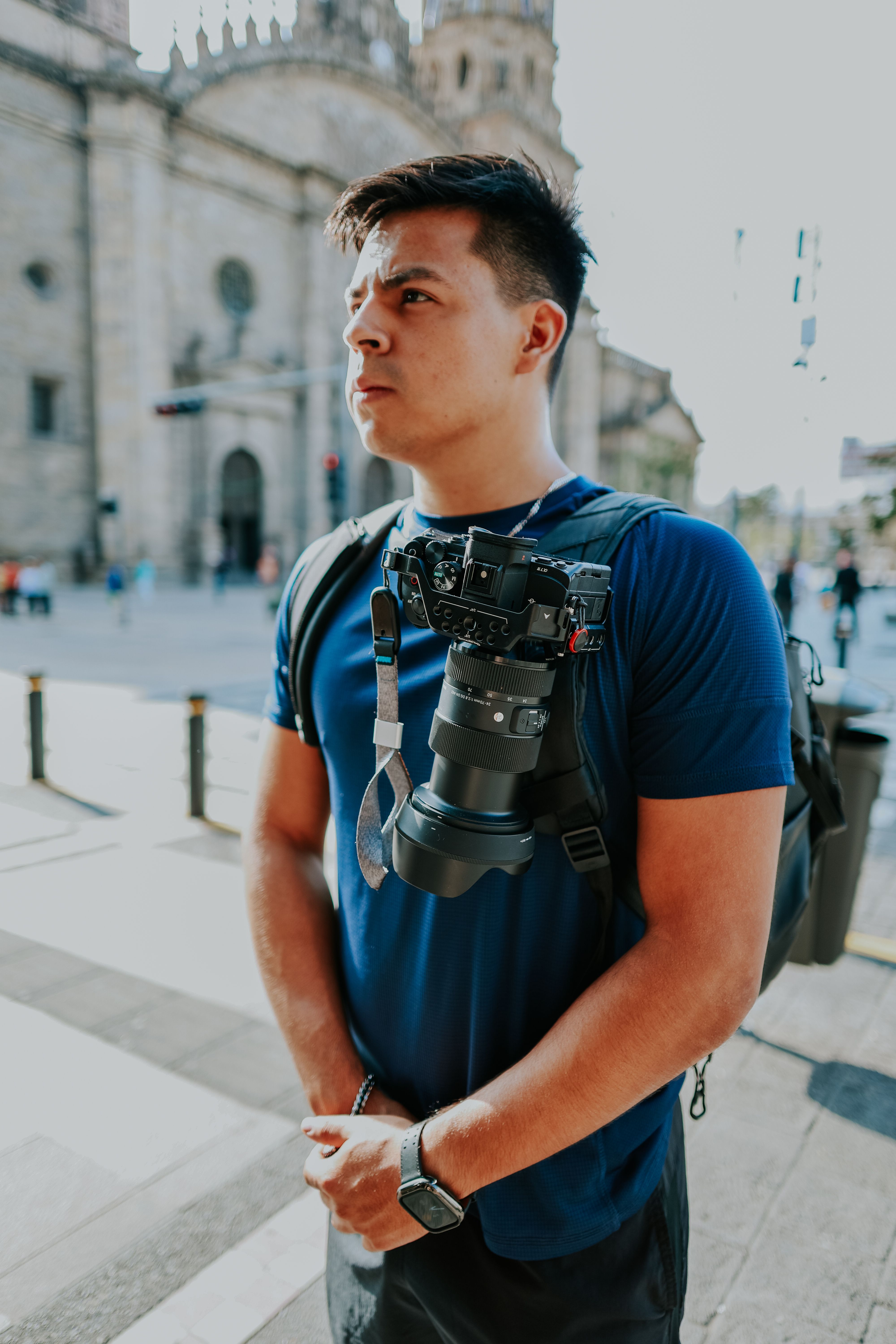 Man in Blue T-Shirt with Camera Attached to Backpack · Free Stock Photo