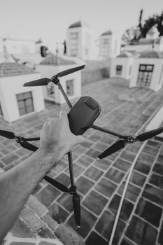 Black and white photo of a hand holding a drone over urban rooftops, creating a modern, tech vibe.