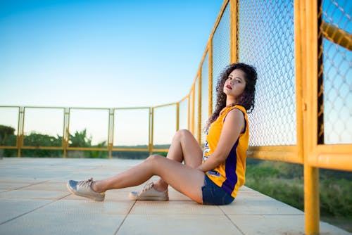 Woman Leaning on Yellow Steel Cyclone Fence