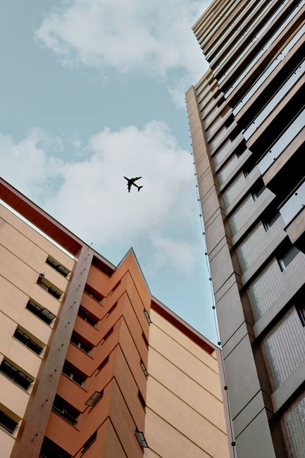 View of skyscrapers with a plane flying above against a blue sky.