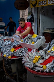 Man in fish market tending to fresh fish display, vibrant urban setting.
