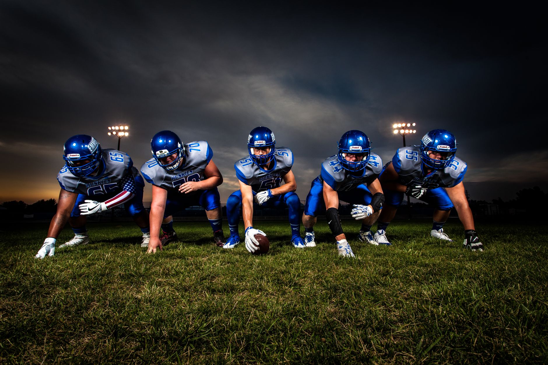 A cohesive football team lines up on the field under stadium lights, prepared for the game ahead.