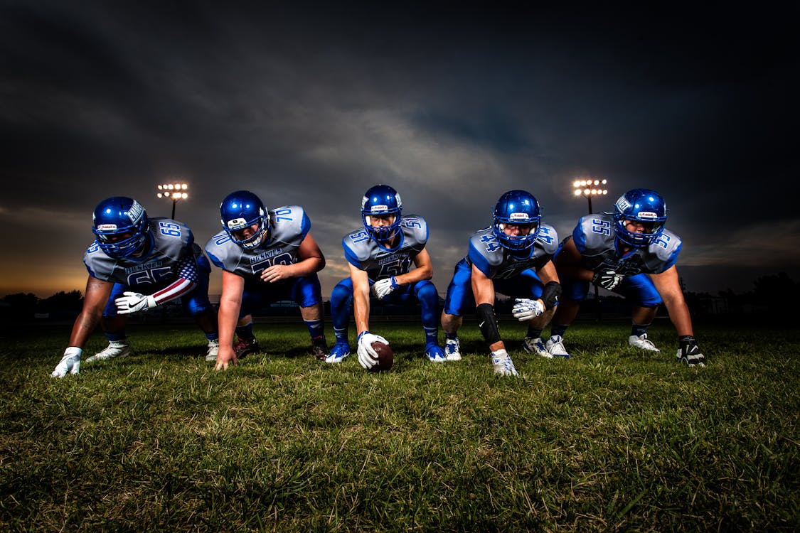 Football Players in Blue Jersey Lined Under Grey White Cloudy Sky during Sunset