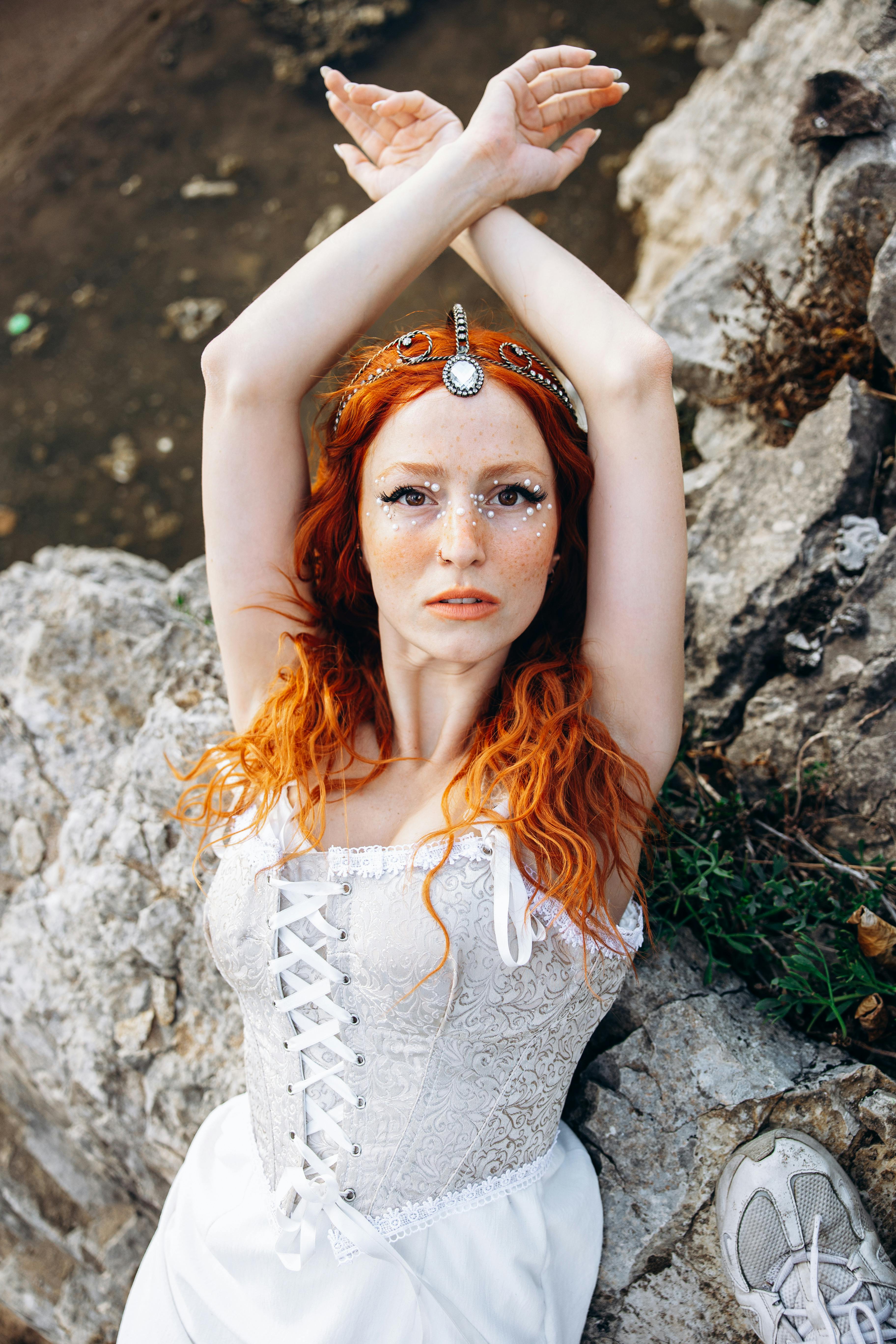 a woman with red hair and white dress is laying on the rocks