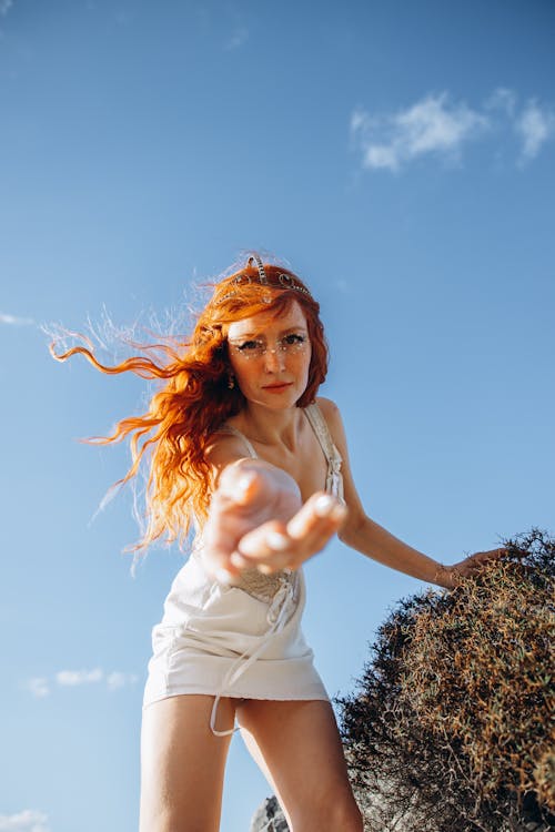 A woman with red hair and white dress is standing on a rock