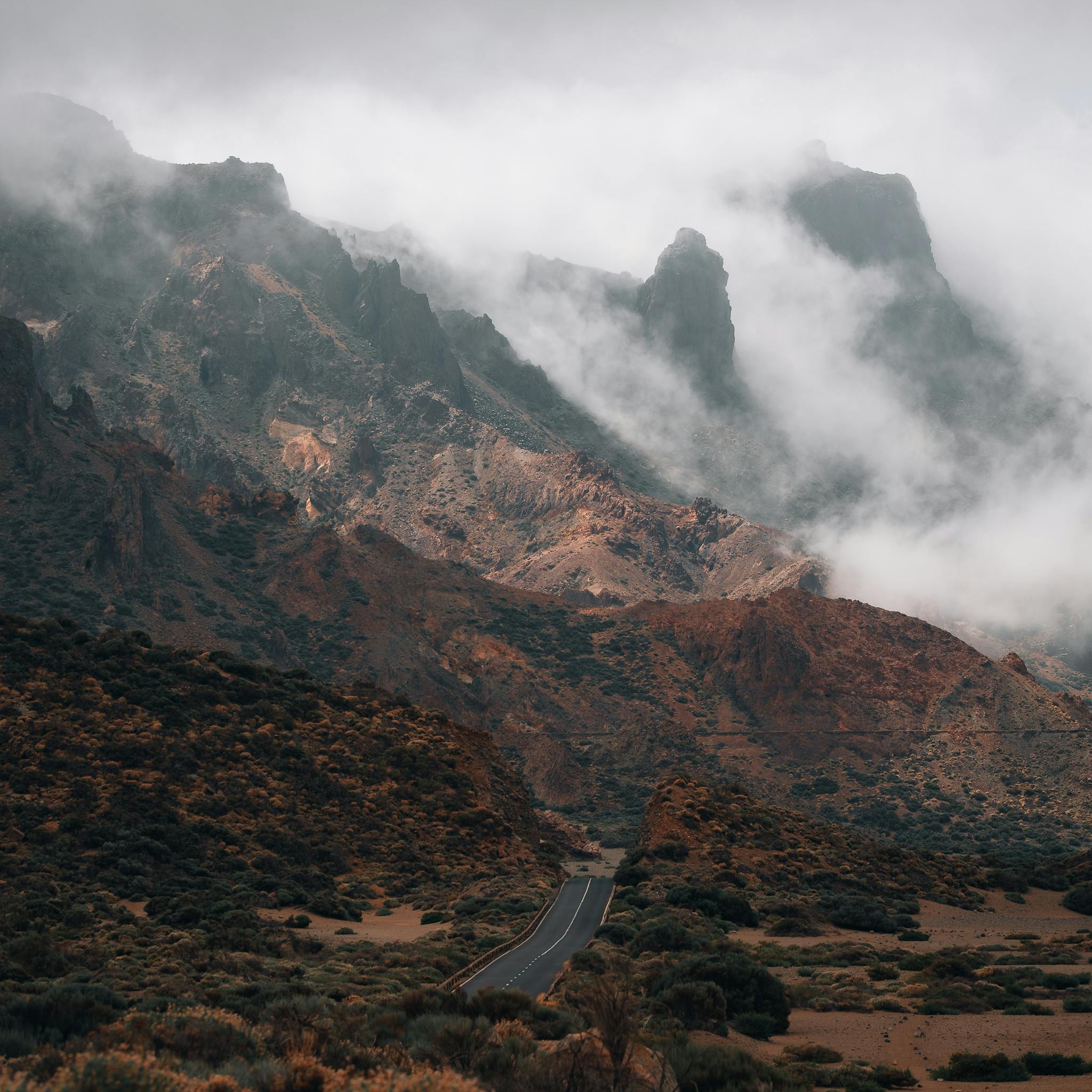 Atmospheric view of a foggy mountain range with a winding road, capturing nature's quiet beauty.
