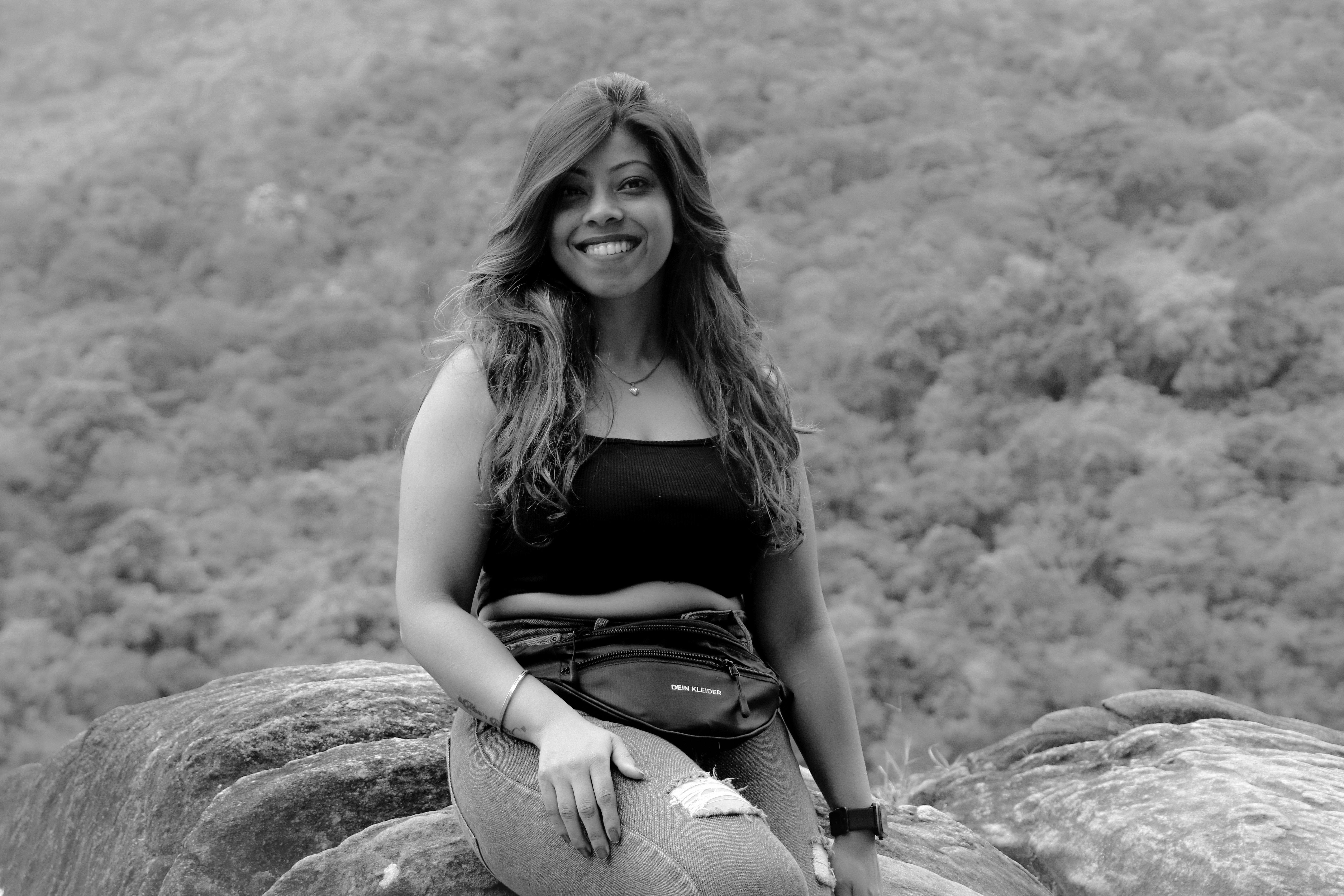 A cheerful woman poses on rocks with a forest background in Madikeri, India.