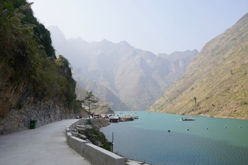 Free A tranquil river surrounded by misty mountains, boats, and a pedestrian walkway. Stock Photo