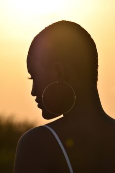 Peaceful silhouette of a woman with hoop earrings against a golden sunset in Accra, Ghana.