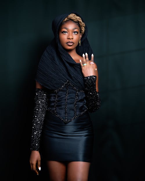 Model in a Black Mini Dress with a Neckline Going Into a Headscarf and Glittery Arm Sleeves