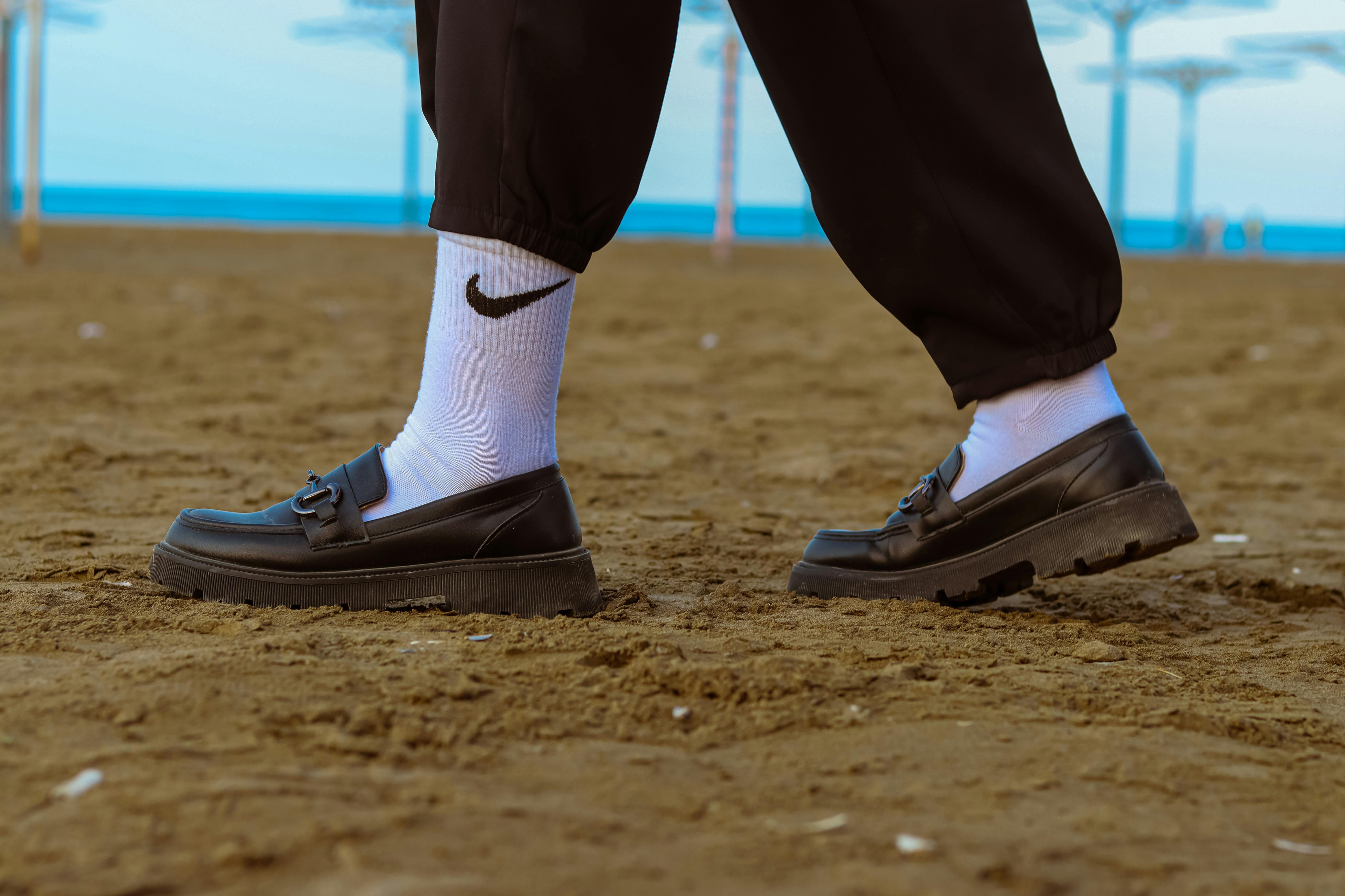 Legs in White Nike Socks and Black Leather Loafers on the Sand