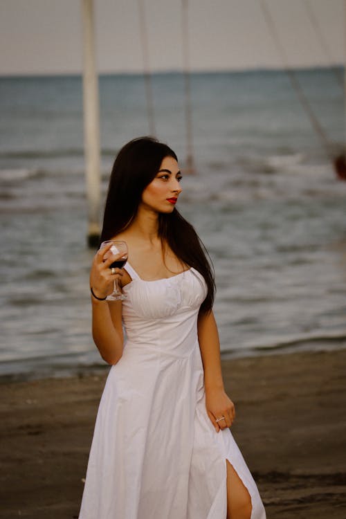Portrait of Brunette Woman in White Dress and with Wine on Beach