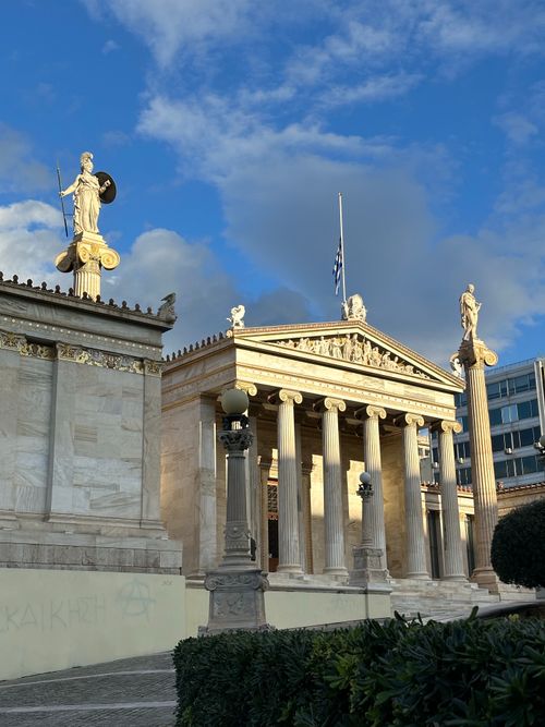 Free Majestic view of the Academy of Athens with classical columns and statues under a vibrant blue sky. Stock Photo