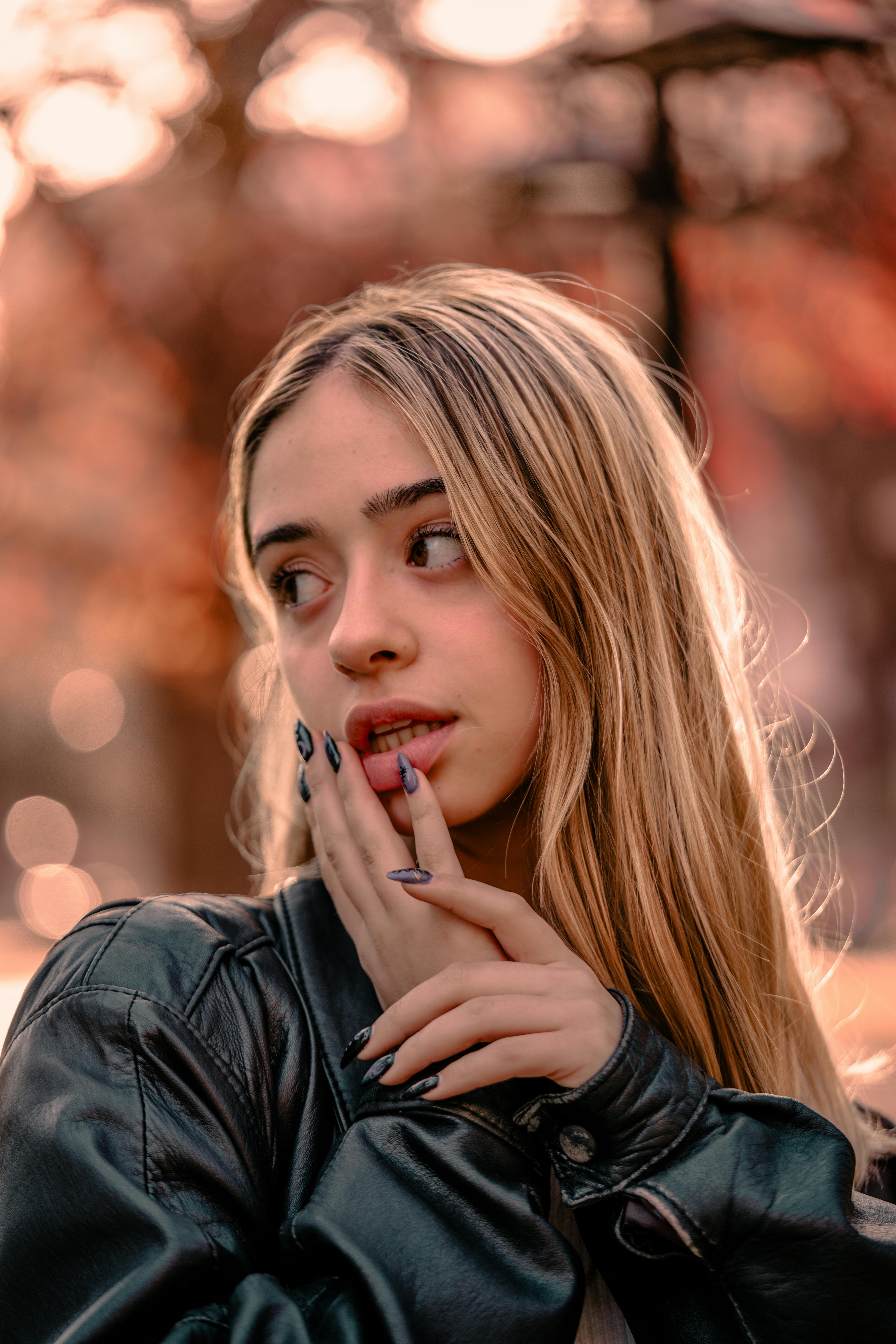 Portrait of a young woman with long blonde hair, wearing a leather jacket, in soft autumn sunlight.