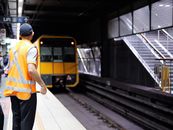 Railway staff in safety vest on platform as train arrives at Sydney station.