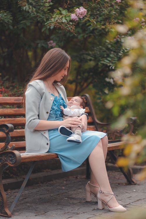Free A mother lovingly holding her baby on a park bench amidst lush greenery during the day. Stock Photo