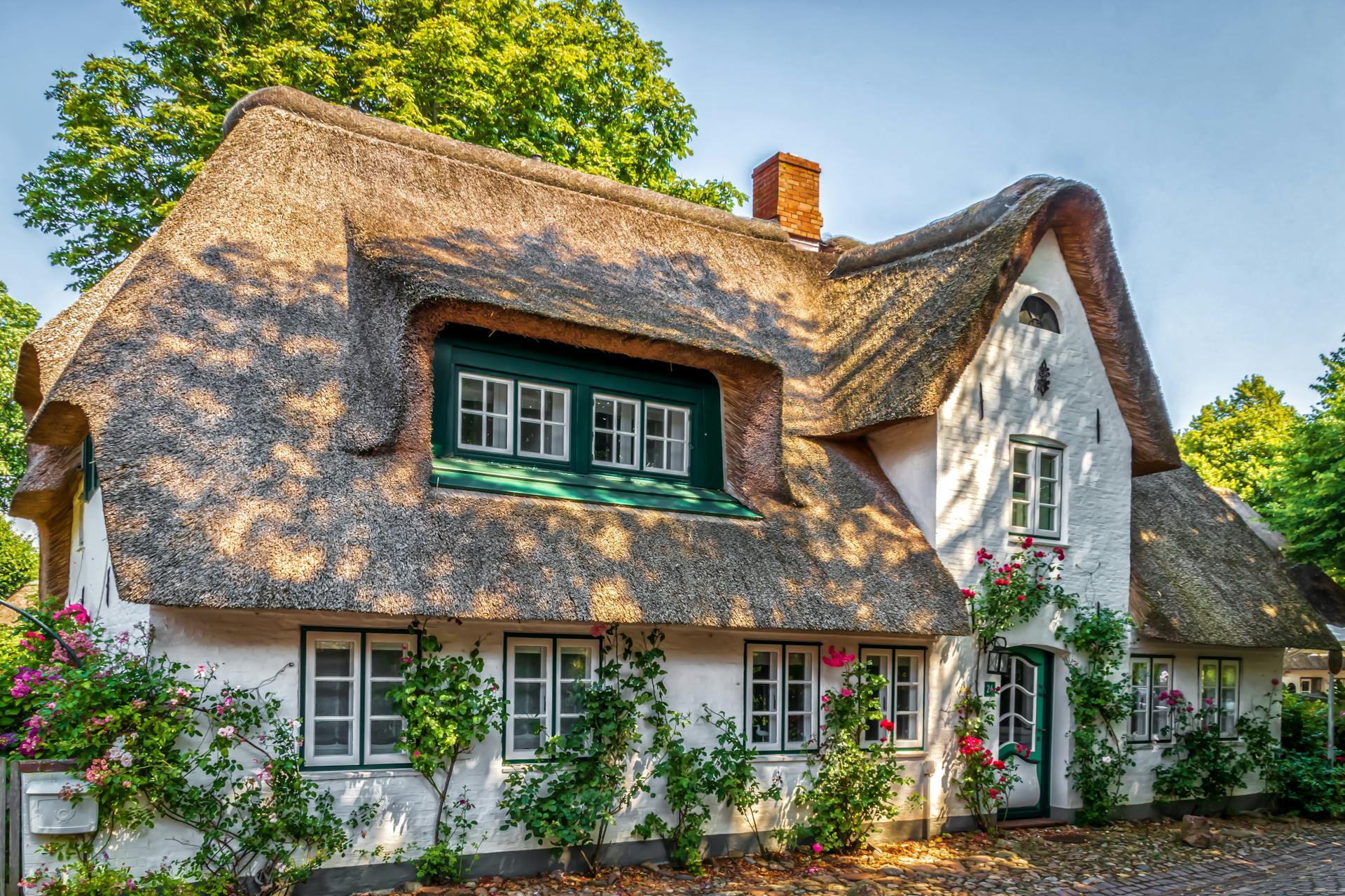 Beautiful thatched roof cottage adorned with flowers and greenery, basking in warm daylight.