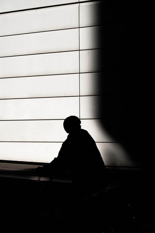 Free Dark silhouette of a person on a bicycle against a bright, modern wall under dramatic lighting. Stock Photo
