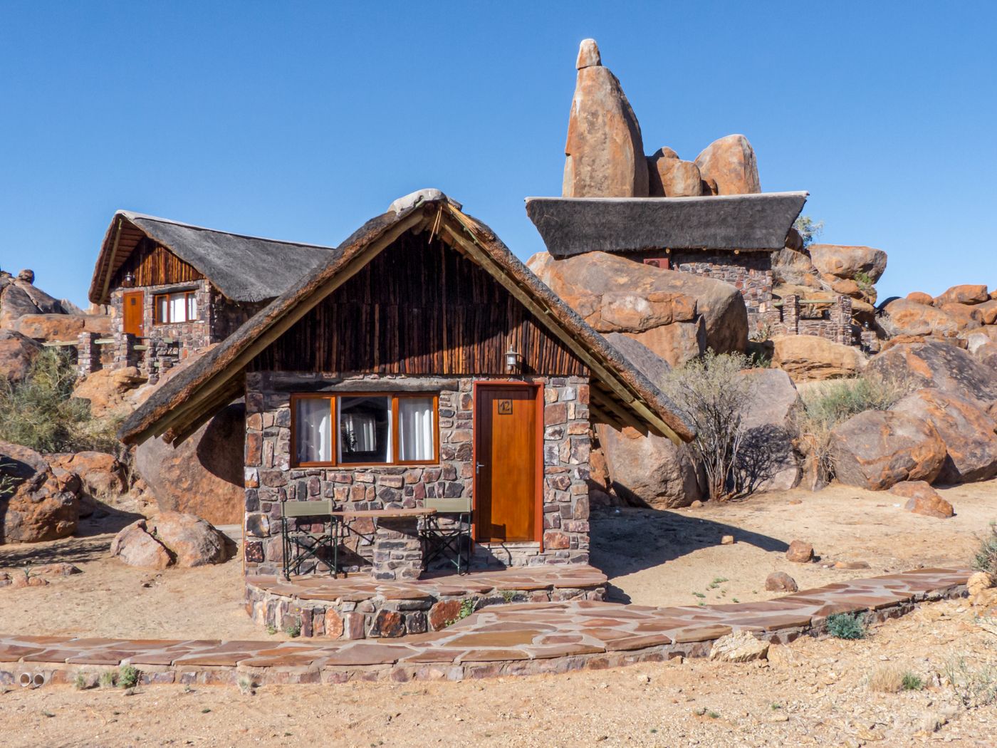 Stone-built lodge huts among large natural rock formations in Namibia's desert landscape