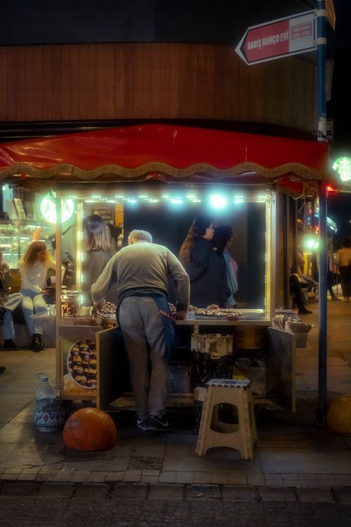 Free A bustling night market scene with a vendor serving customers under warm glowing lights. Stock Photo
