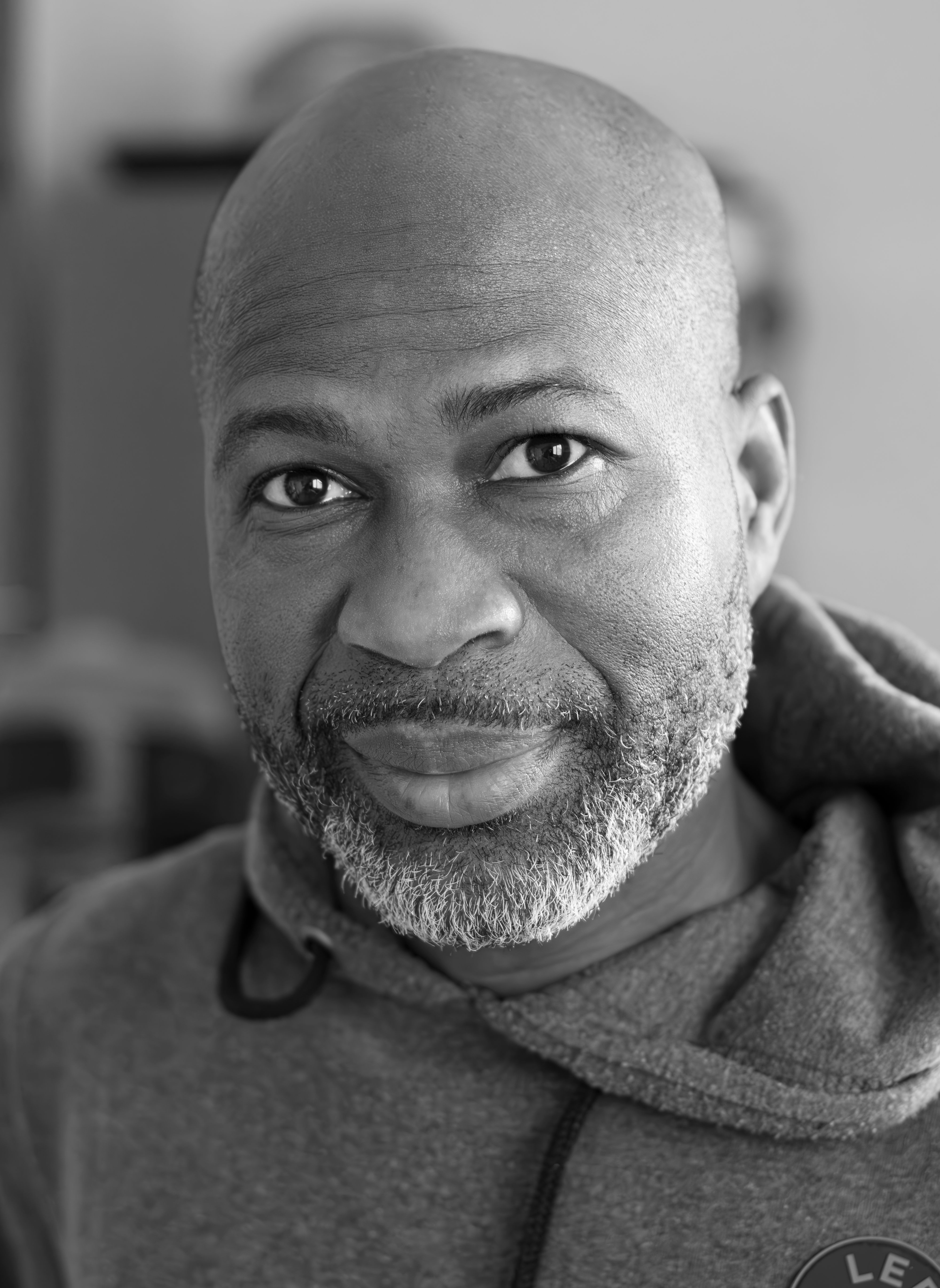 A serious bald man with a bearded face wearing casual clothing in a black and white portrait.