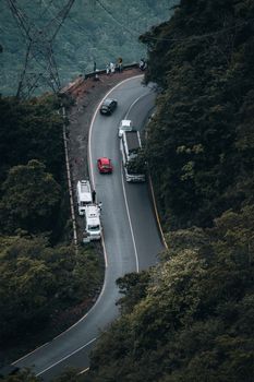 A bird's eye view of a mountain road with vehicles navigating a sharp curve through lush greenery.