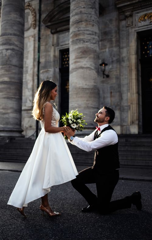 Free Man proposing to woman with bouquet in elegant street setting. Stock Photo