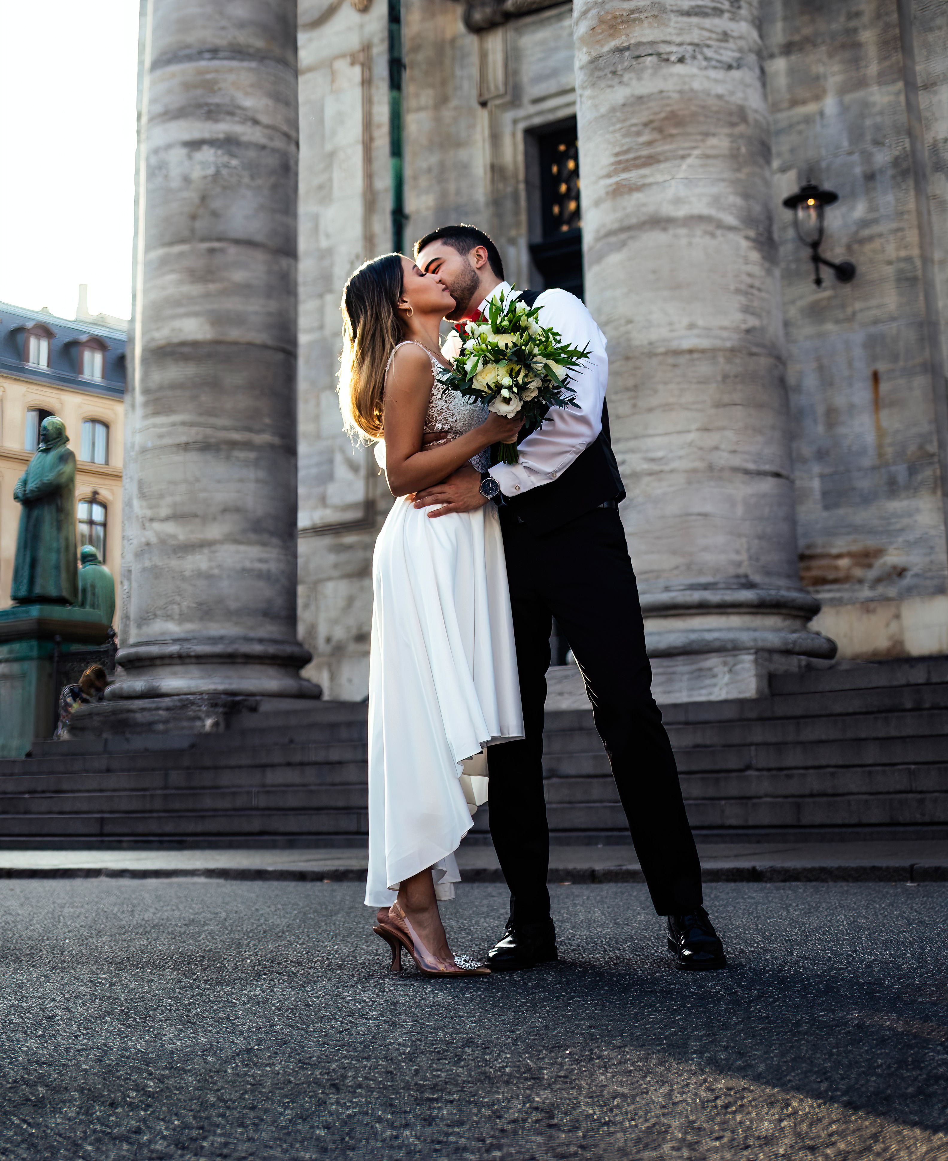 A bride and groom kiss in front of a large building · Free Stock Photo