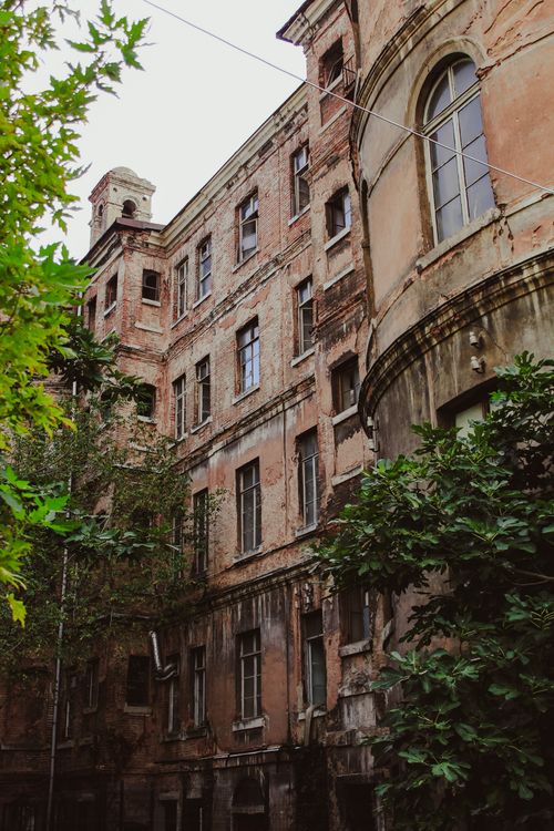 Free A decaying urban building surrounded by overgrown trees and foliage, showcasing architectural neglect. Stock Photo