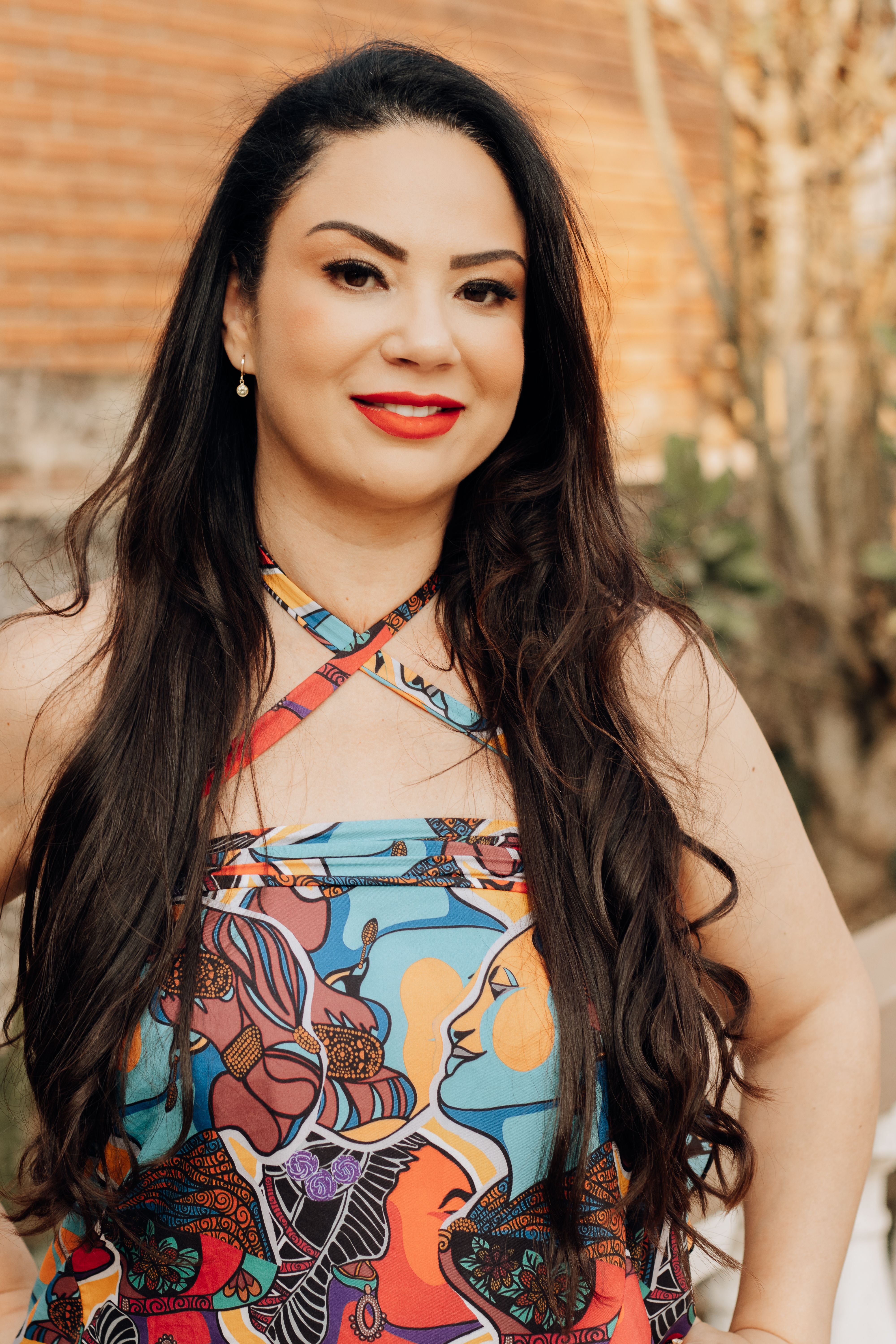 Elegant portrait of a woman in a vibrant dress with artistic patterns, standing outdoors.