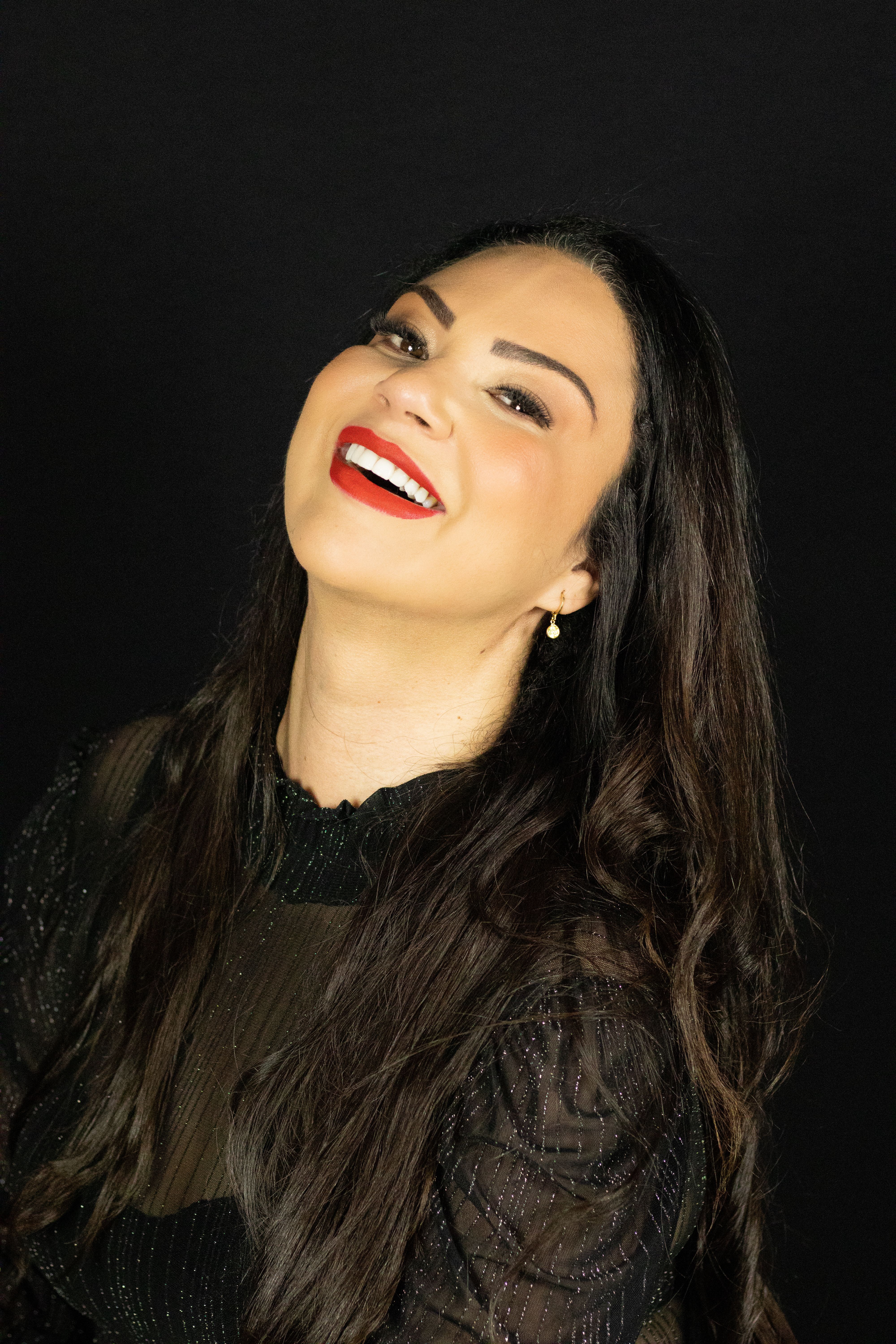 A glamorous studio portrait of a smiling woman with long hair and bright red lipstick.