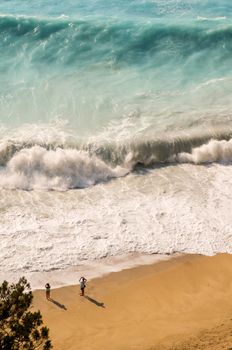 A breathtaking aerial view of a beach in Lefkada, Greece with crashing waves and two people enjoying the scenery.