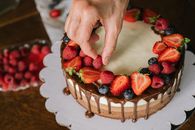 Hand placing fresh berries on a chocolate-covered cake, creating a delicious dessert.