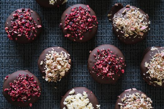 Assorted chocolate bites topped with dried berries on a textured surface.
