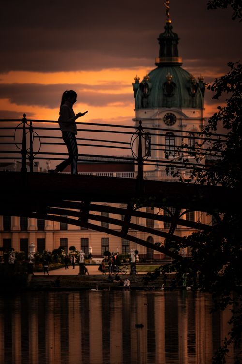 Free A woman walks across a bridge with an architectural dome in the background during sunset. Stock Photo