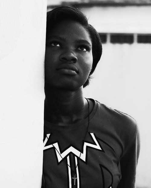 Free Black and white portrait of a young woman standing by a wall, gazing upwards, creating a serious and contemplative mood. Stock Photo