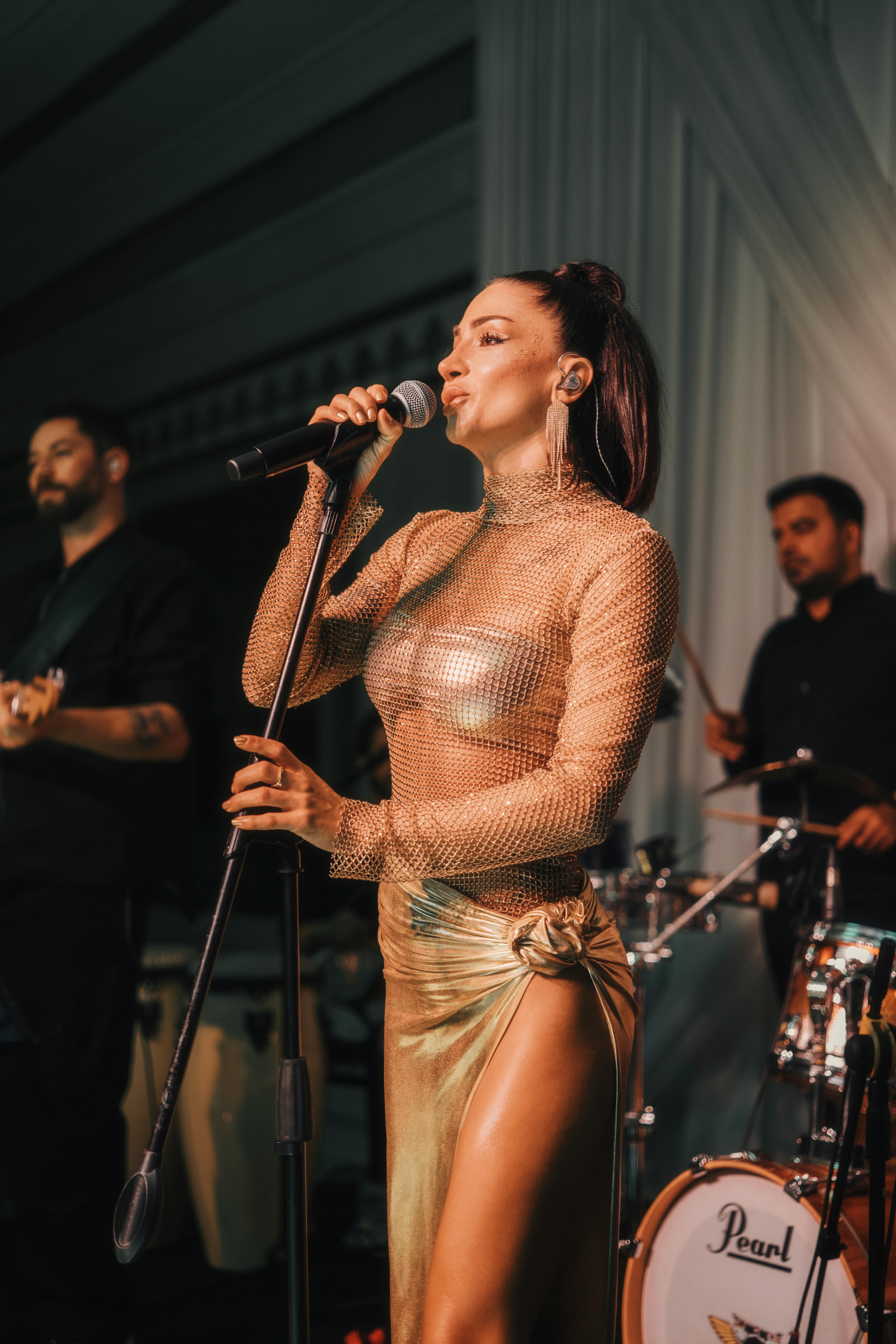 a woman in a gold dress singing into a microphone