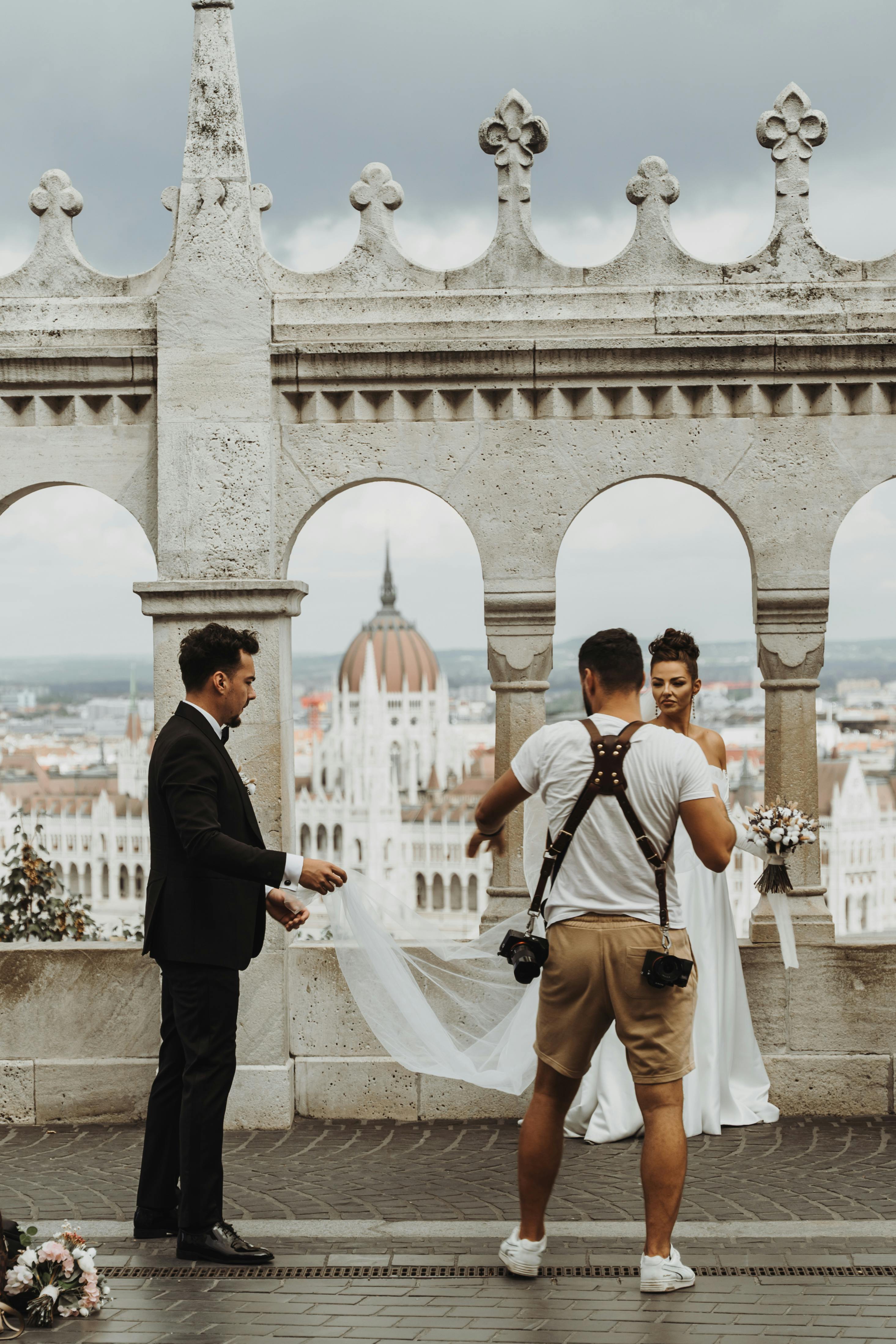 A stunning wedding photoshoot at Fisherman's Bastion in Budapest, featuring a bride, groom, and their photographer.