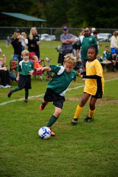 Boys and girls in team soccer jerseys playing soccer on a green field outdoors.