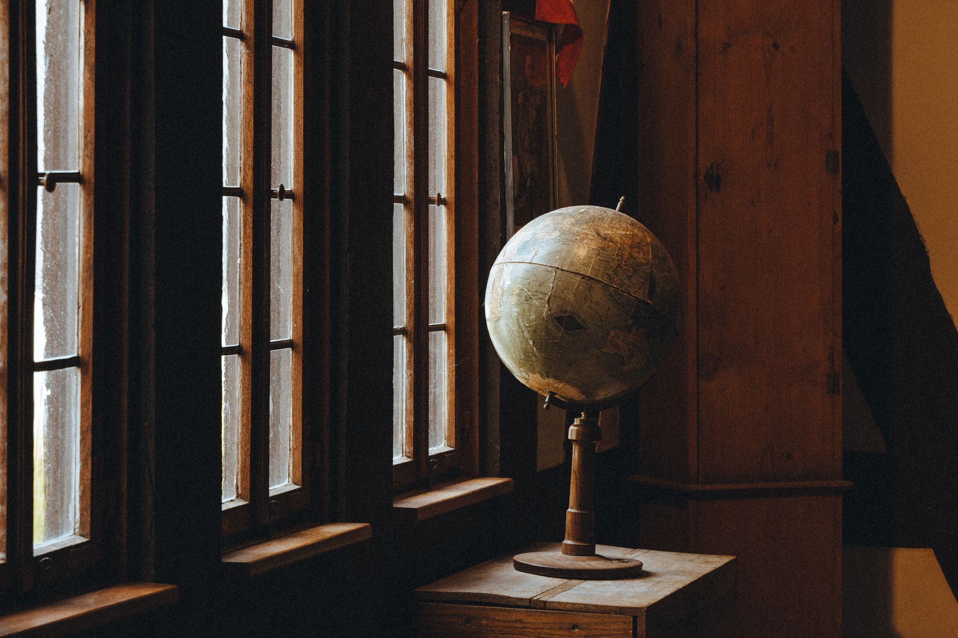 A vintage globe sits by a rustic window, bathed in warm light and shadow.