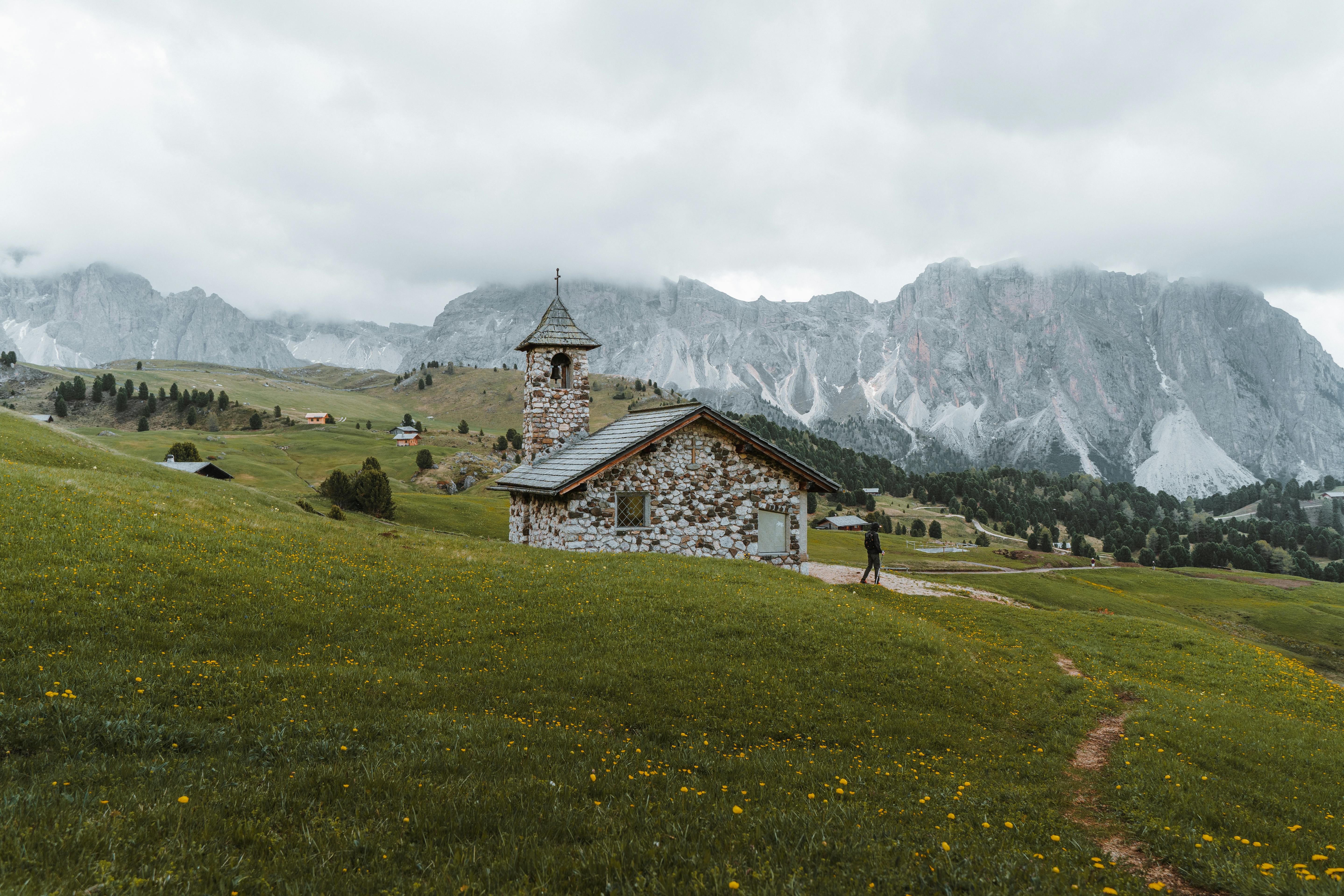 Charming stone house amidst green meadows and foggy mountains, perfect for travel inspiration.