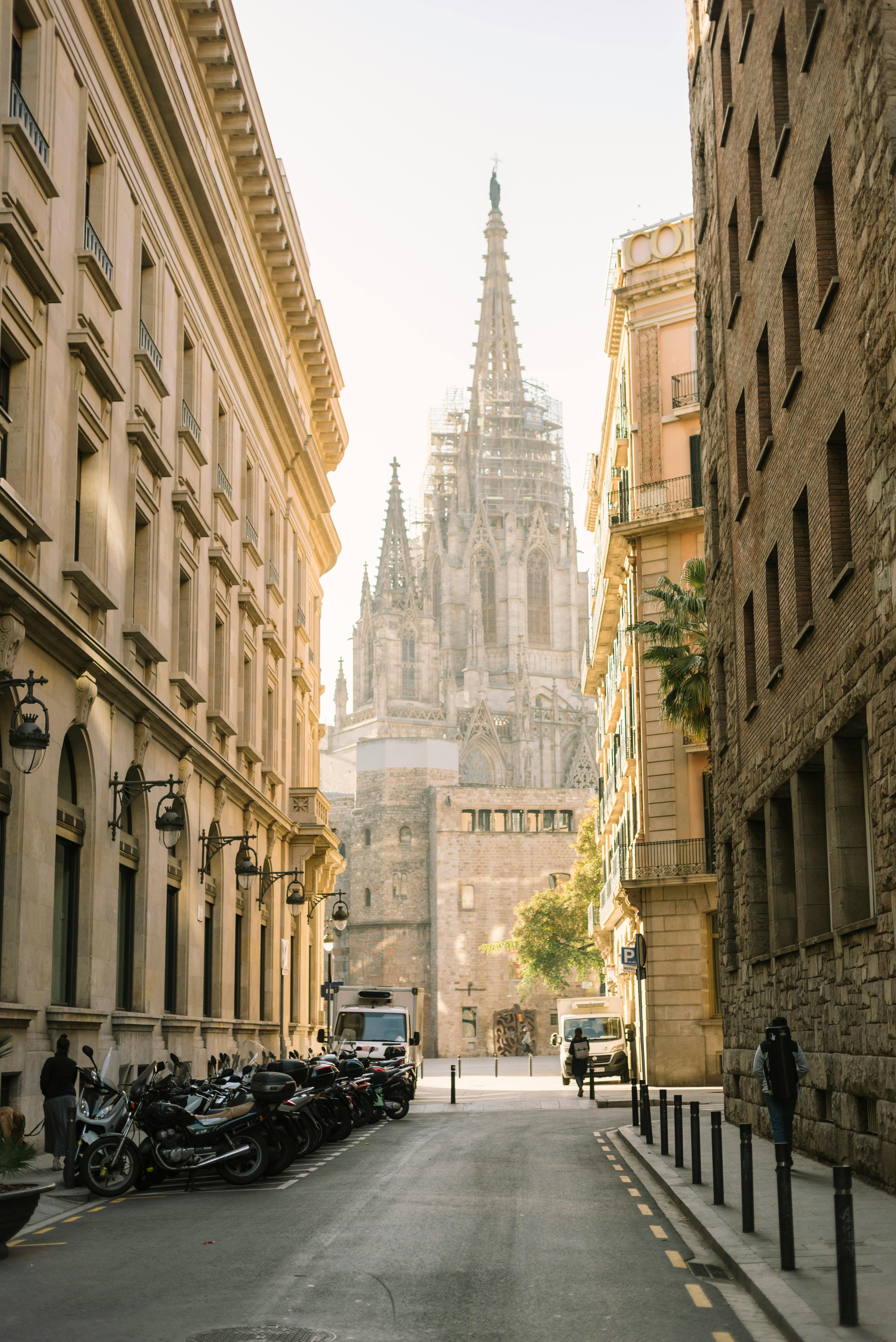 View of a gothic cathedral with intricate architecture framed by urban buildings under sunlight.