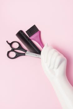 Scissors, comb, and brush displayed creatively on a pink backdrop