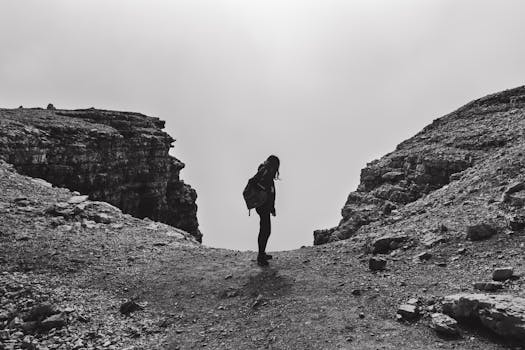 Black and white photo of a woman hiking at Passo Pordoi, capturing a dramatic mountain scene.