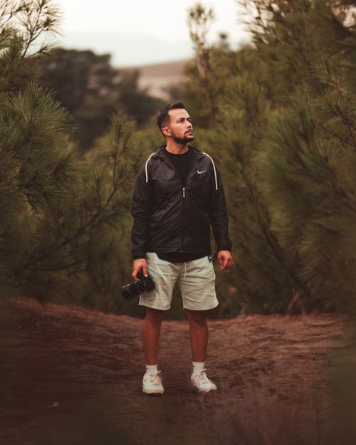 Free A man stands holding a camera, exploring the forest in a black jacket. Stock Photo