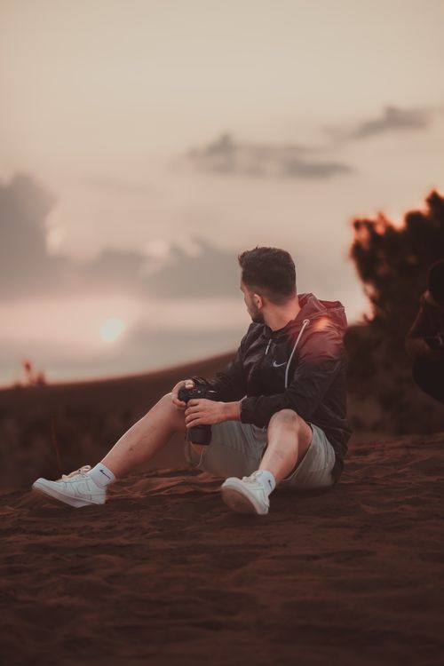 Free A man sits on a hillside capturing a stunning sunset with his camera. Stock Photo