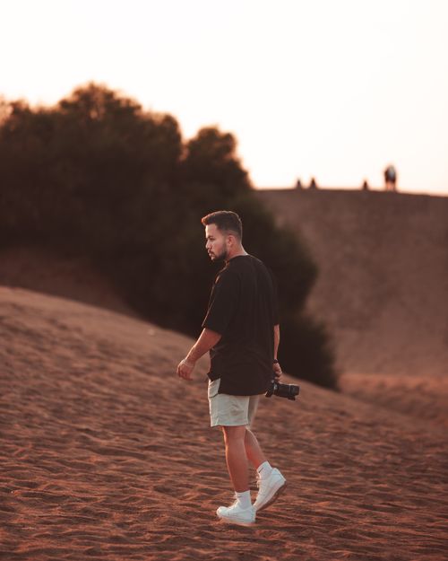 Free A photographer in white sneakers walks across a sandy desert landscape during sunset, holding a camera. Stock Photo