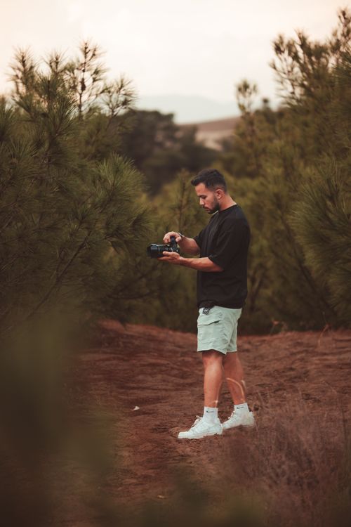 Free A man stands among trees in a forest using a camera, capturing nature's beauty. Stock Photo