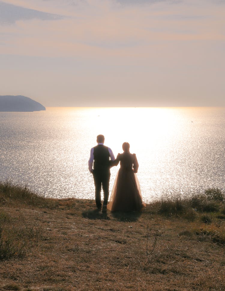 Couple Standing Together On Hill Over Shiny Sea Shore At Sunset